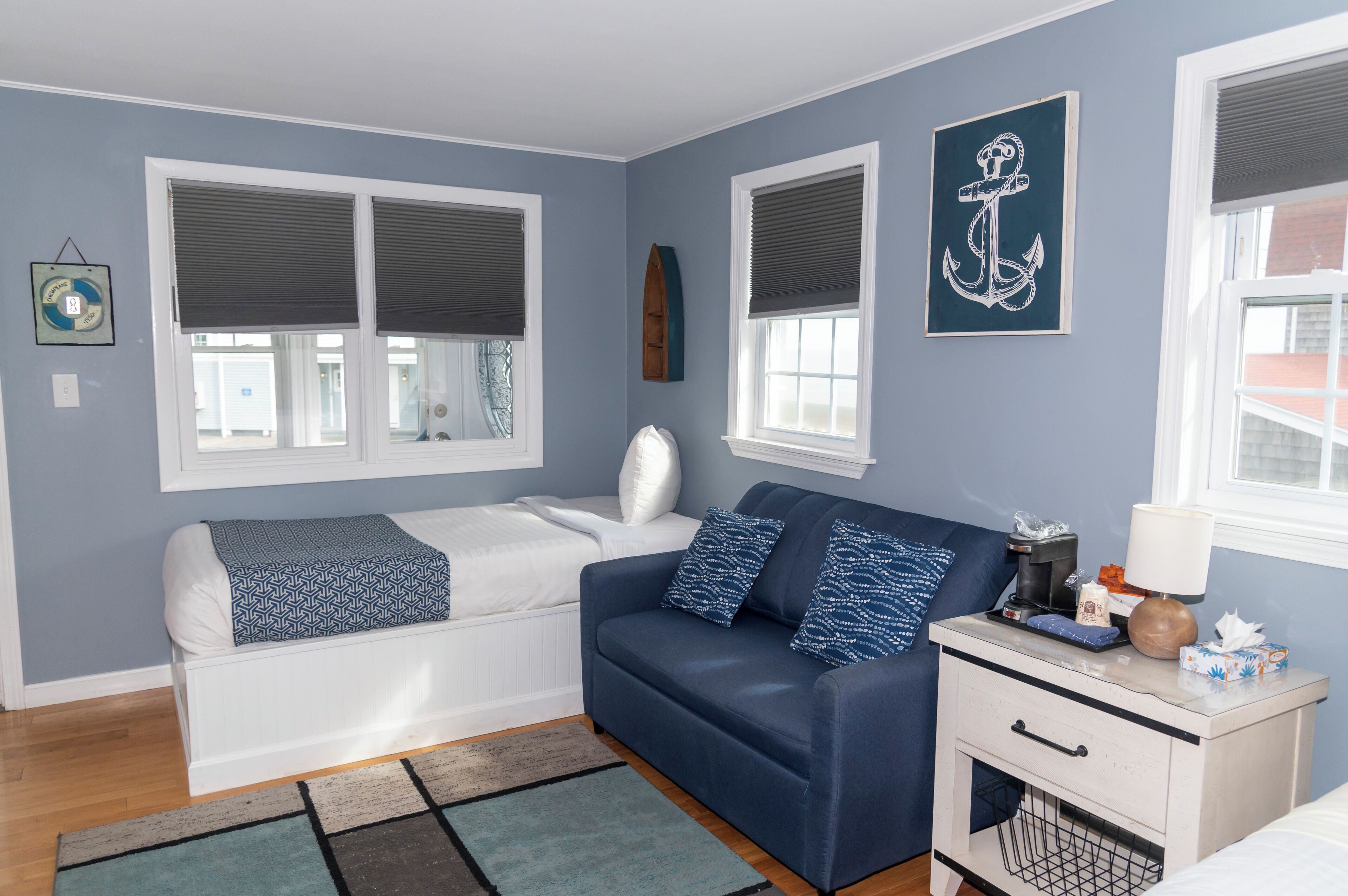 A room with a bed, a sofa, a nightstand, and a window with blinds.