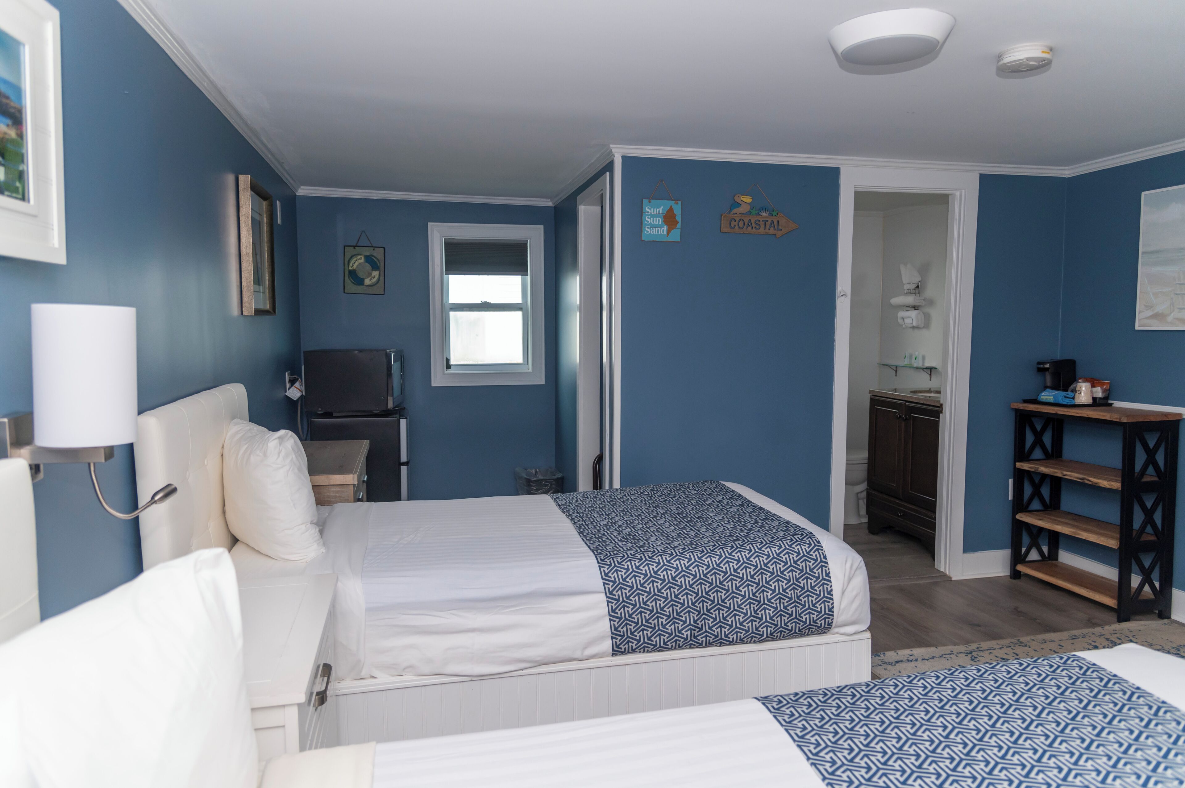 A bedroom with two beds, a television, a small desk, and a bathroom visible through an open door.