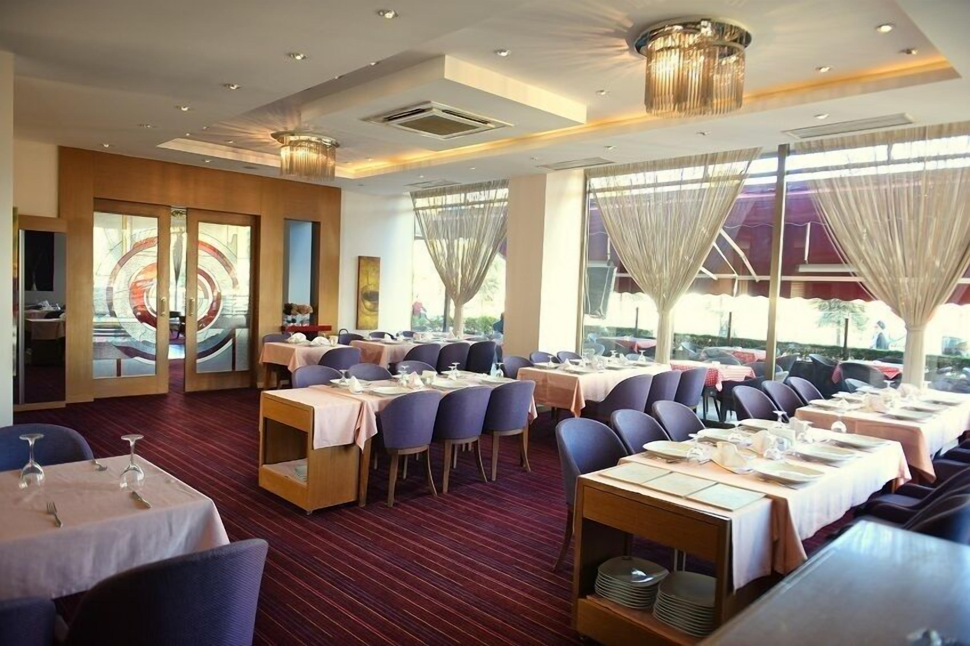 A restaurant with multiple dining tables, chairs, and a large window with curtains.