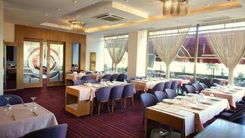 A restaurant with multiple dining tables, chairs, and a large window with curtains.