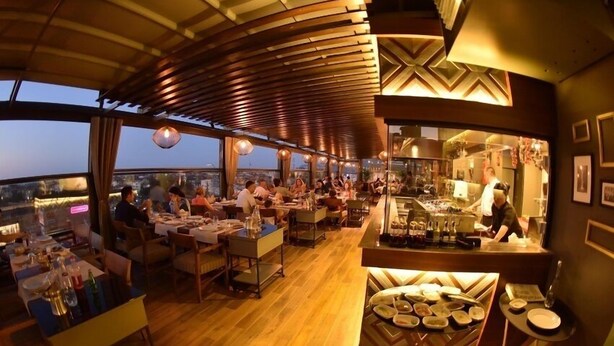 A restaurant with a modern interior, wooden ceiling, and a view of the cityscape. - Baliktasi City Hotel (Ordu)