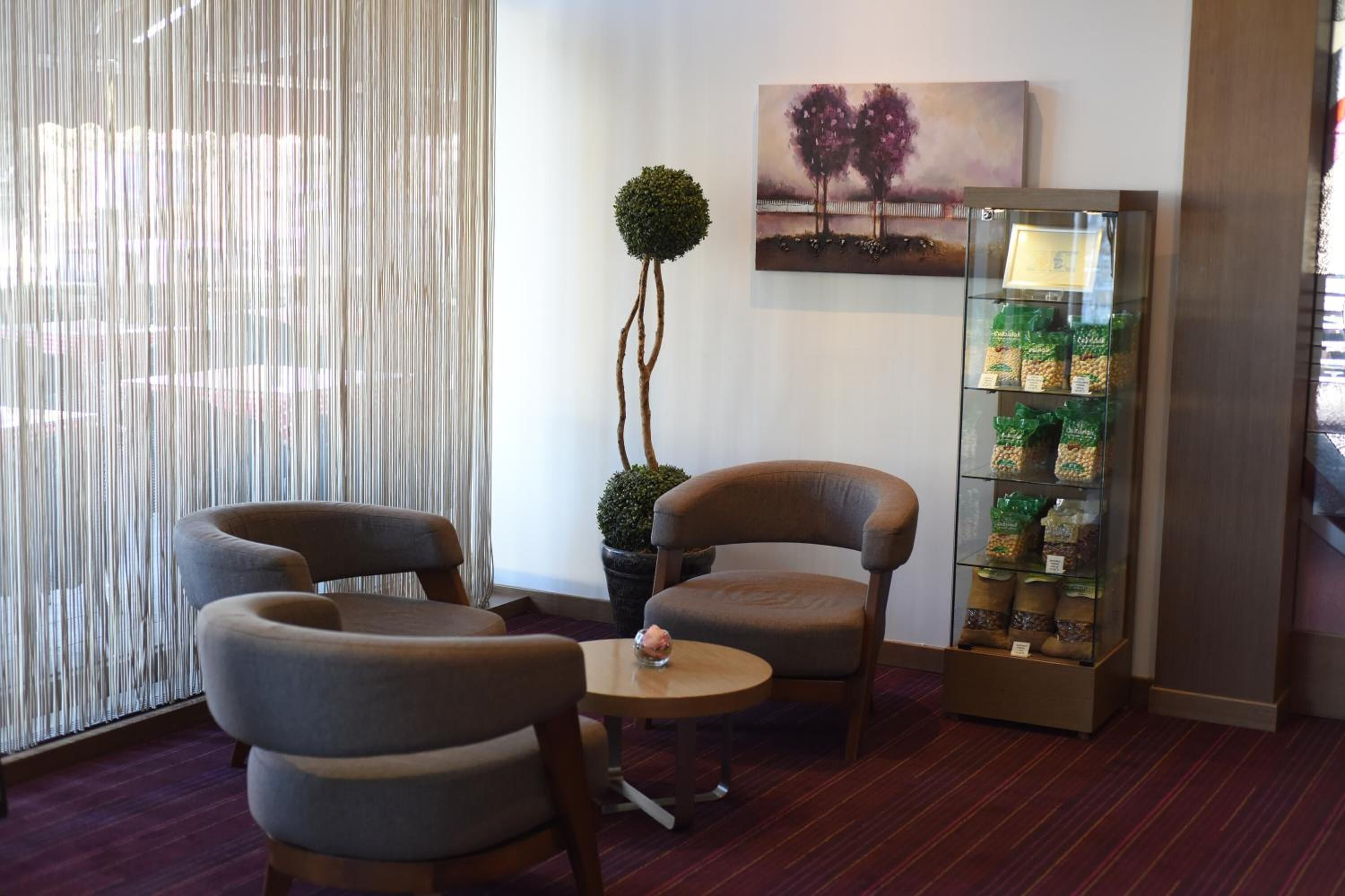 Eine Hotellobby mit zwei Sesseln, einem kleinen runden Tisch, einem Blumentopf, einem Gemälde und einer Snackauslage.