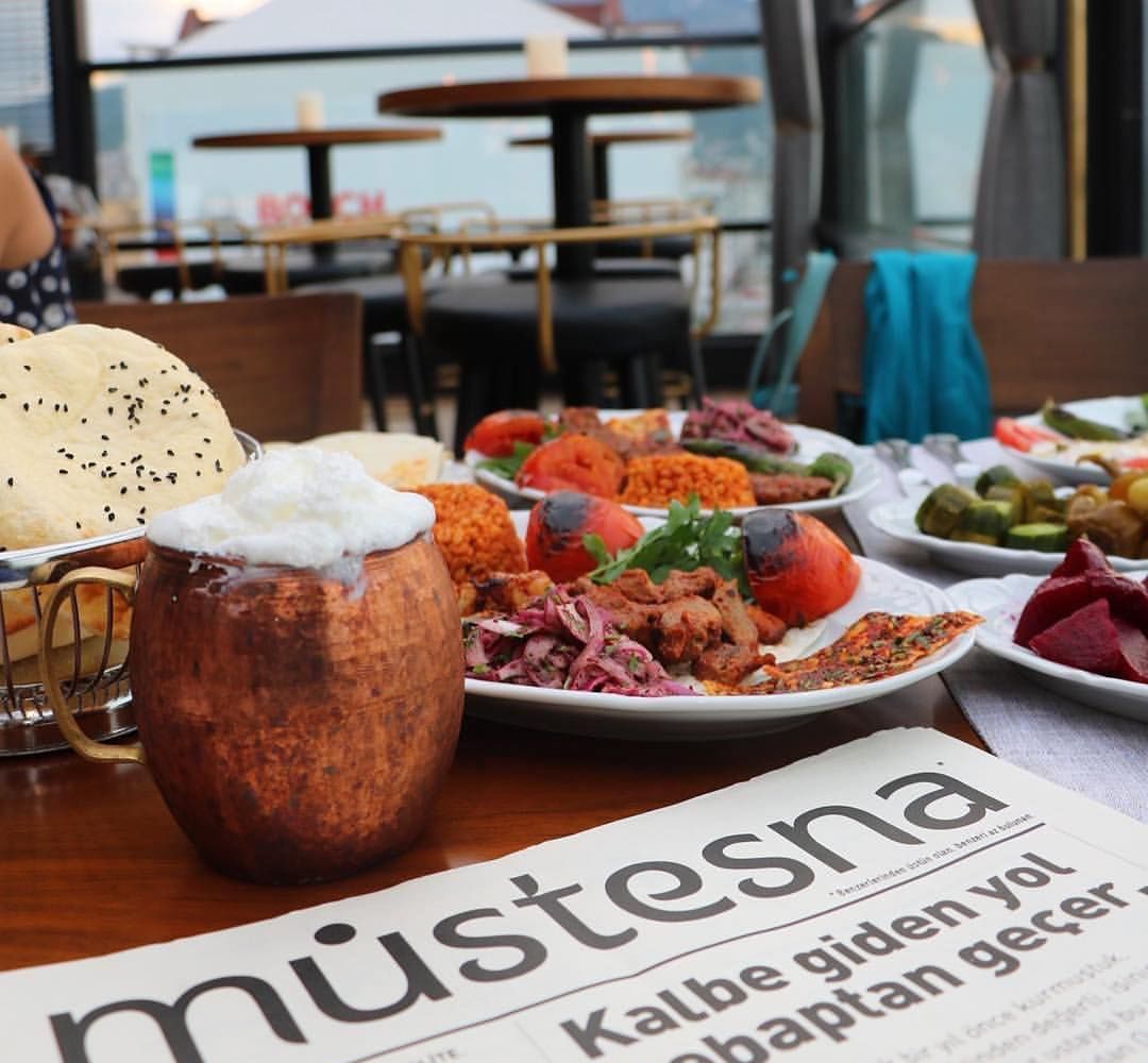 A table with various dishes, a copper mug, and a menu titled "Mütesna".