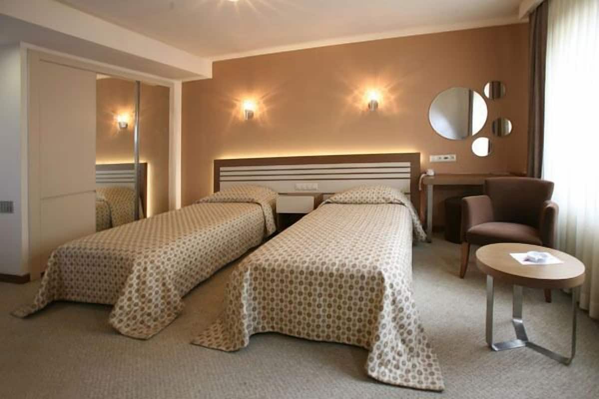 Ein Hotelzimmer mit zwei Einzelbetten, einem Schreibtisch, einem Stuhl und einem kleinen Tisch.