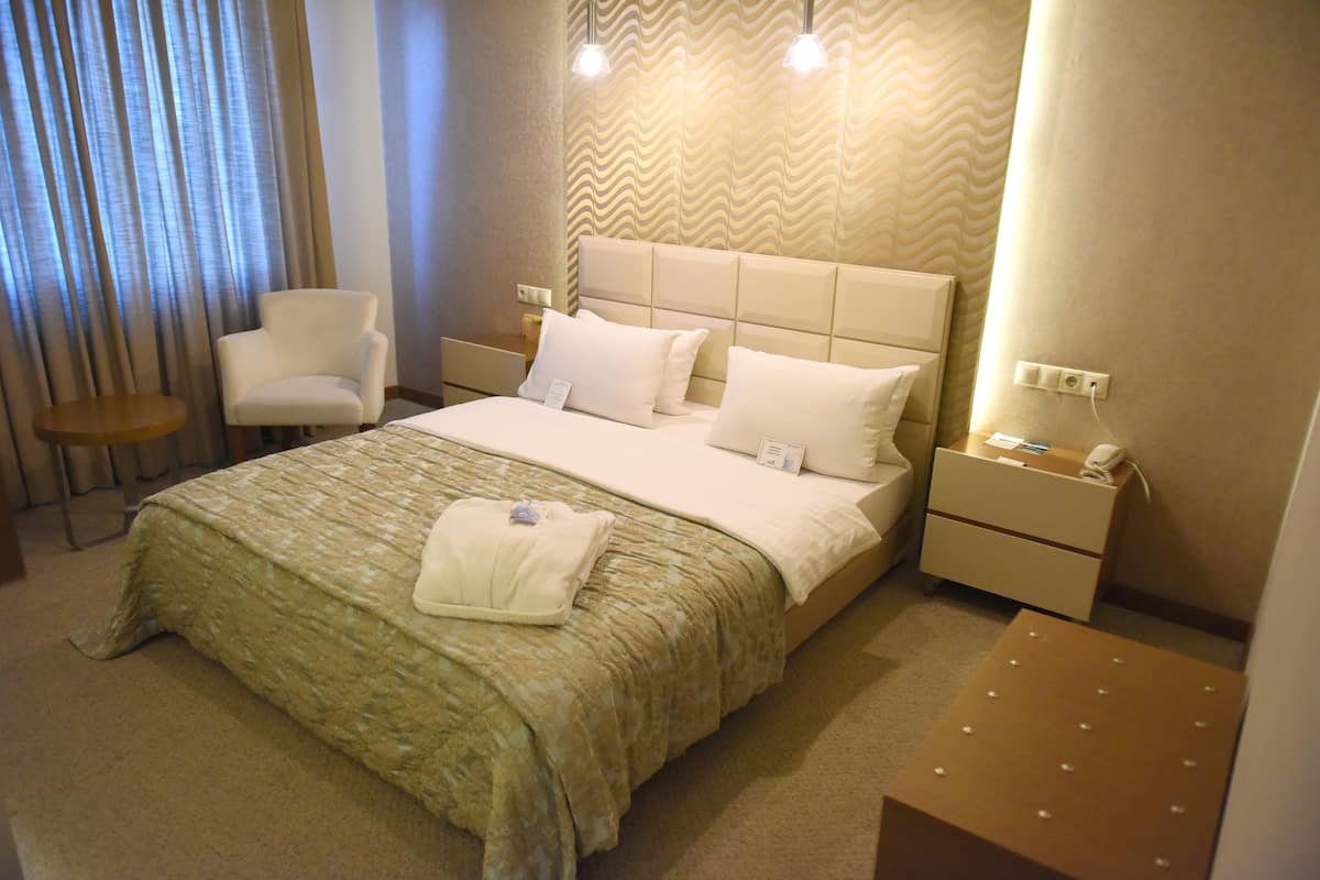 Ein Hotelzimmer mit einem großen Bett, einem Nachttisch, einem Sessel und einem kleinen Tisch.
