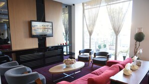 A modern living room with a red sofa, grey armchairs, a coffee table, and a flat-screen TV mounted on the wall. - Baliktasi City Hotel (Ordu)