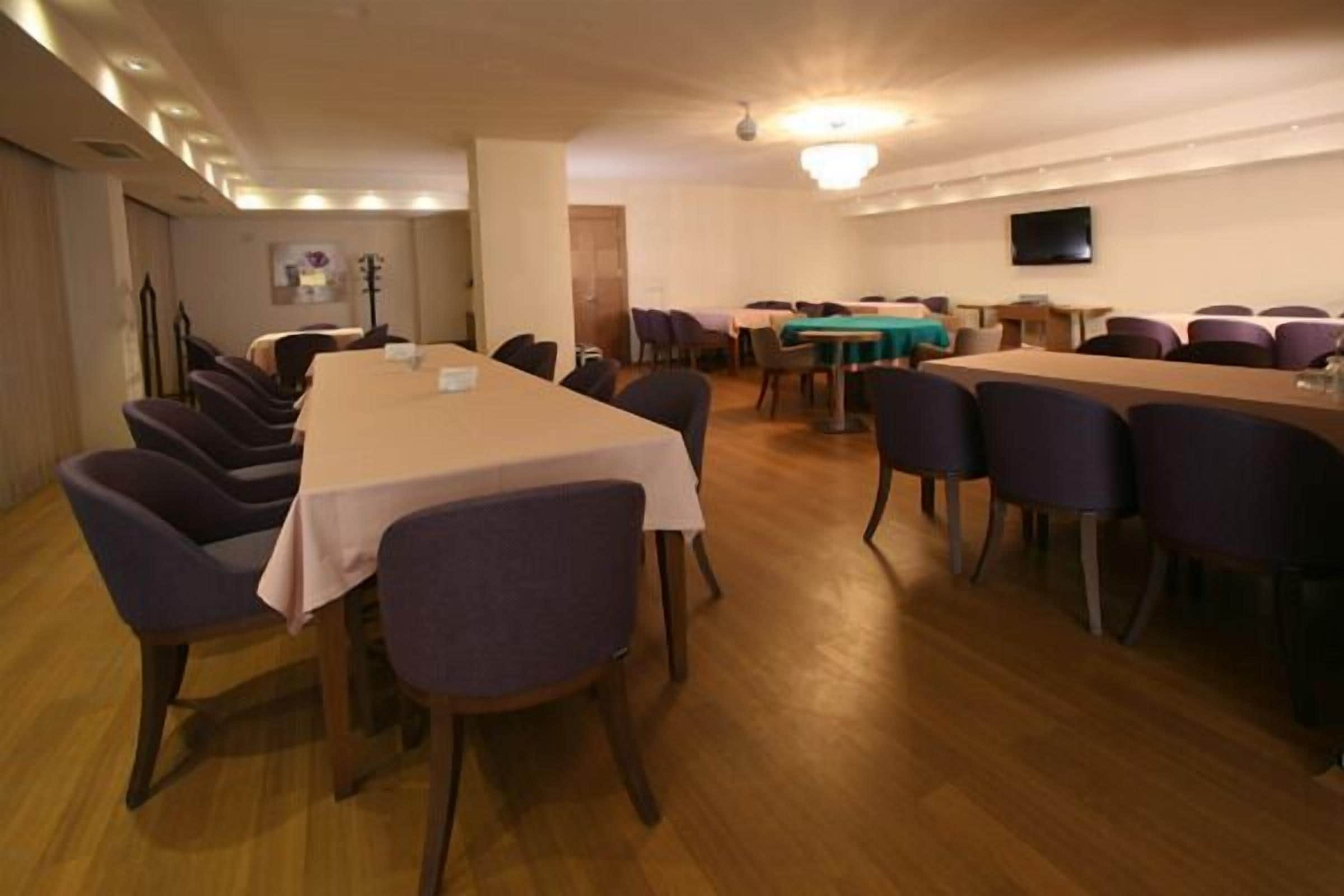 A conference room with multiple tables and chairs, a chandelier, and a flat-screen TV on the wall.