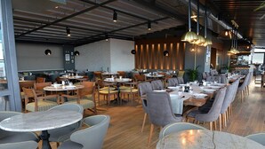 A modern restaurant with round tables and chairs, a brick wall, and hanging pendant lights. - Baliktasi City Hotel (Ordu)
