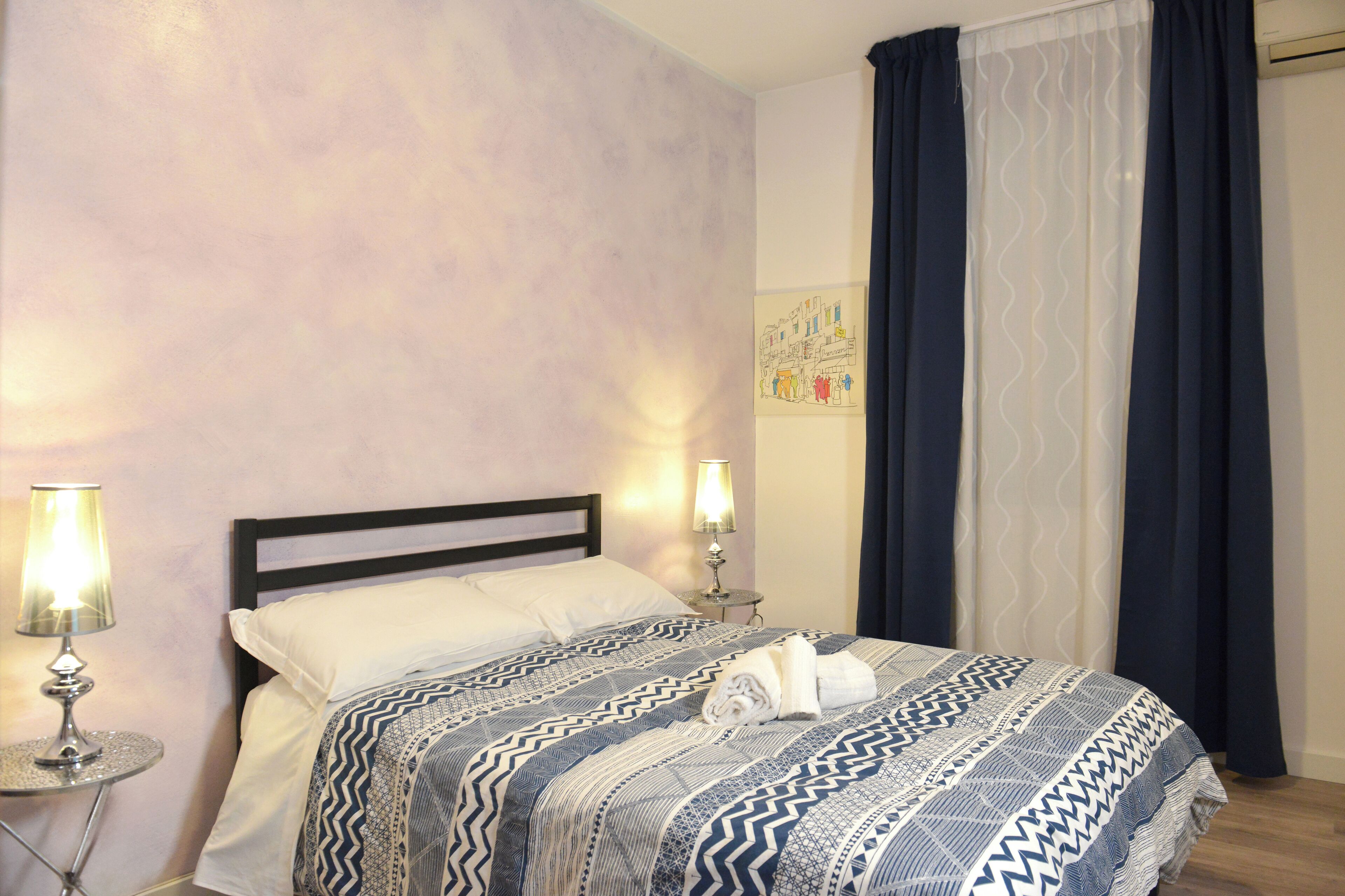 A neatly made bed with a patterned bedspread, two bedside lamps, and a wall art piece.