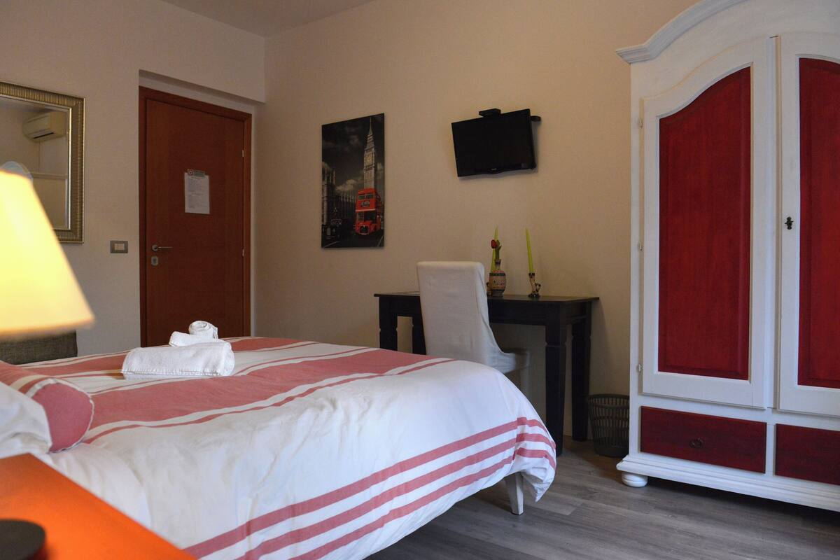 Habitación de hotel con cama, escritorio, silla, armario y un cuadro en la pared.