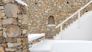 A stone staircase leading up to a white door, with a stone wall and a small arched window. - Cova Mykonos Suites (Mykonos)