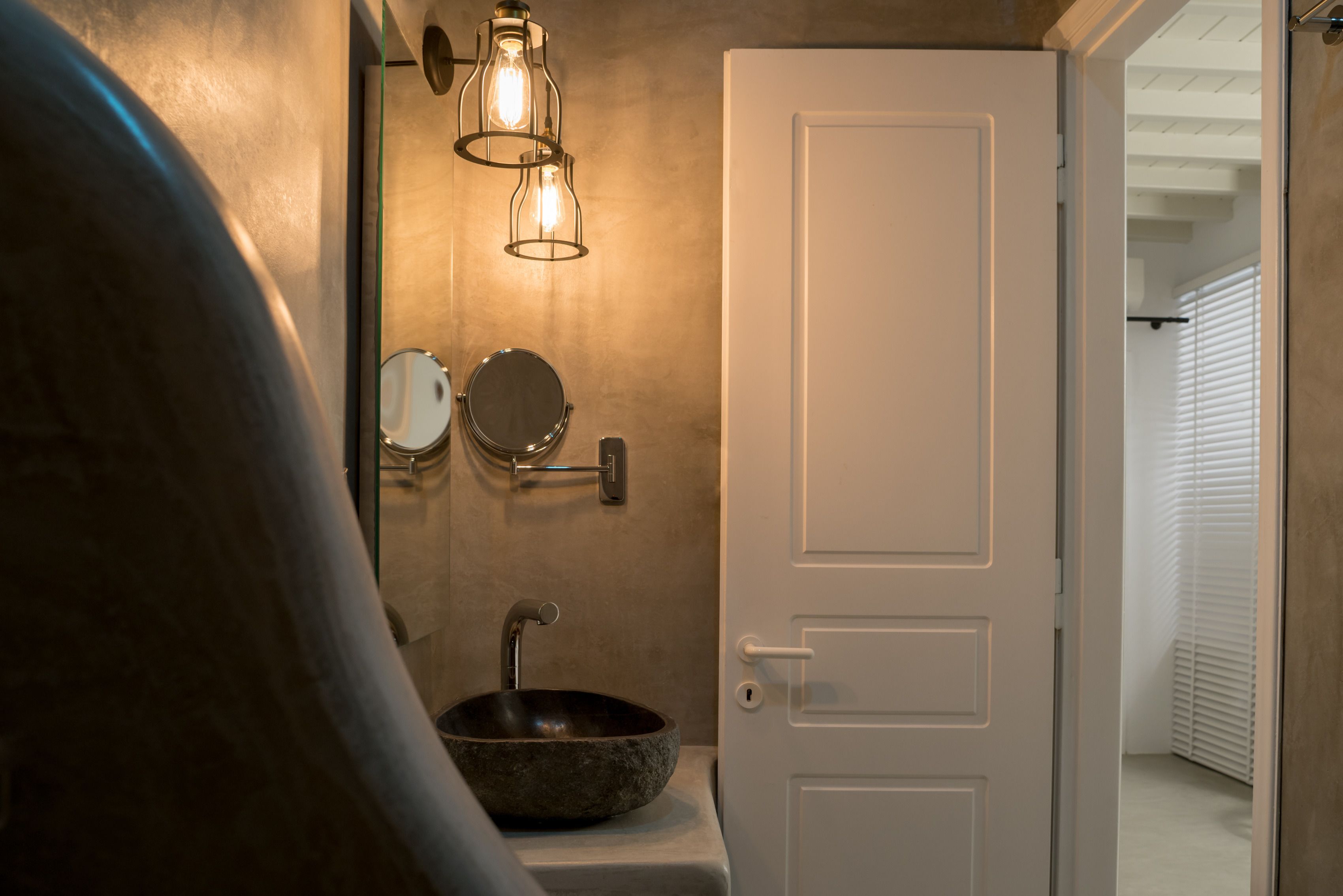 Un baño con un lavamanos de piedra, dos espejos y una puerta que da a otra habitación.
