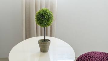 A round white table with a potted plant, wooden legs, and two knitted poufs in red and black.