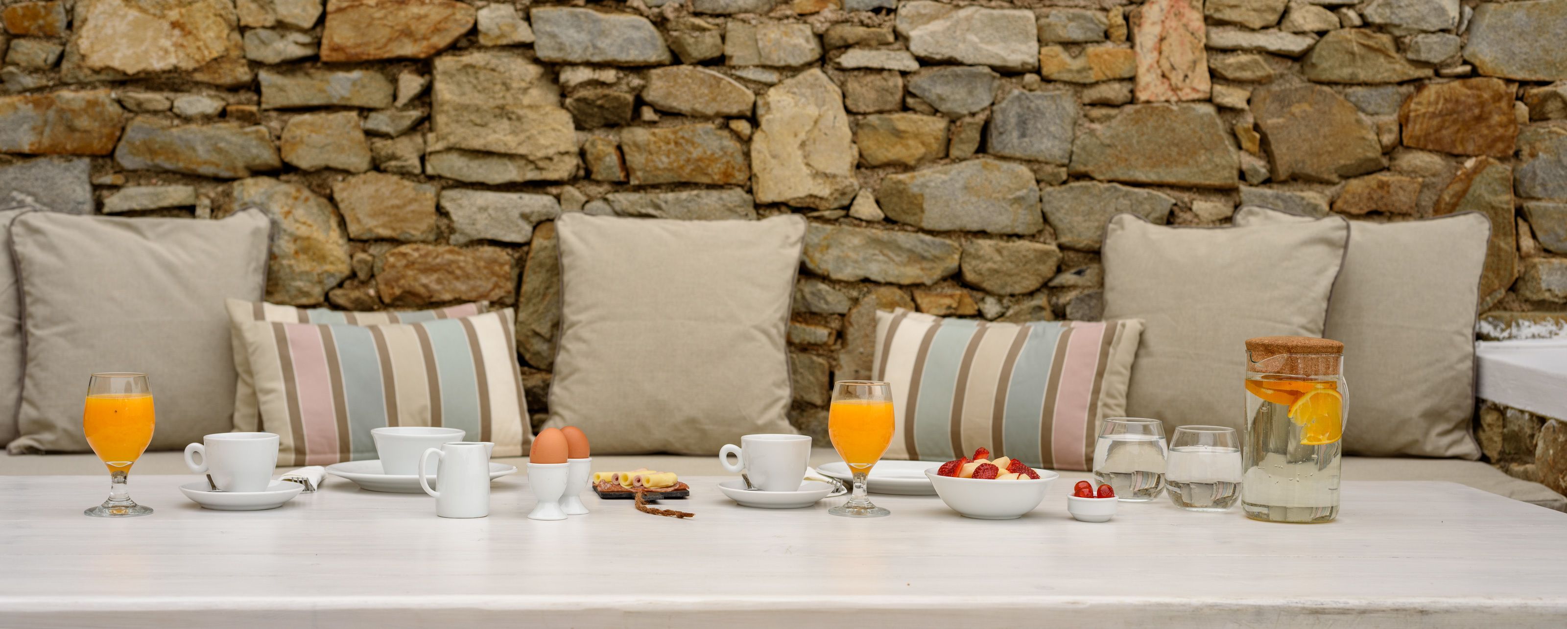A breakfast setup with a stone wall background, white tableware, and a variety of breakfast items.