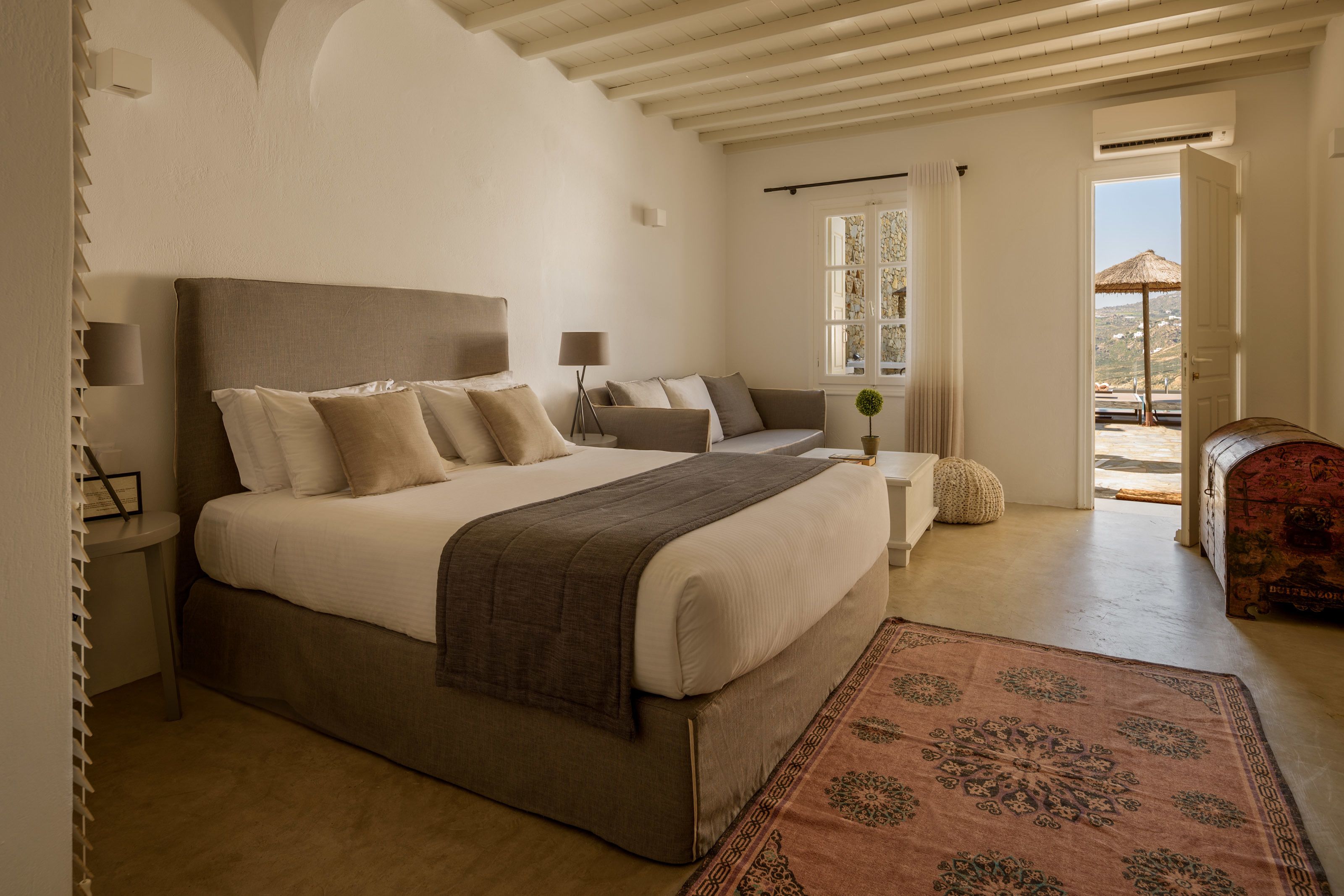 A bedroom with a large bed, bedside tables, a sofa, and a view of the outdoors.