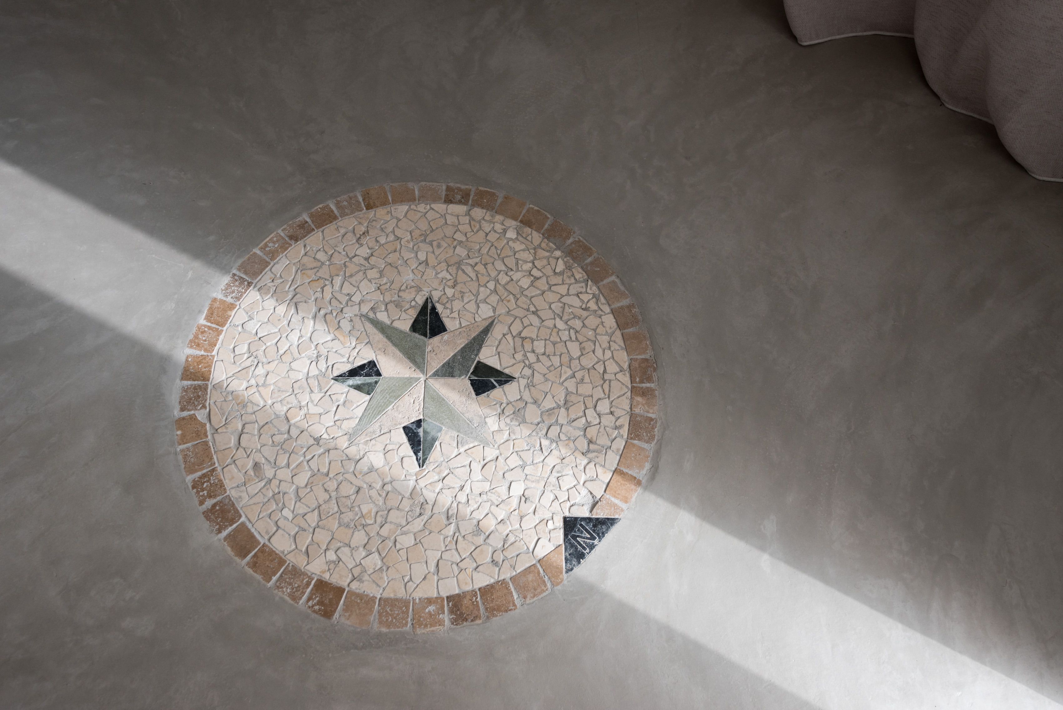 Un suelo de mosaico circular con un diseño de brújula, rodeado por un borde de baldosas marrones y beiges.