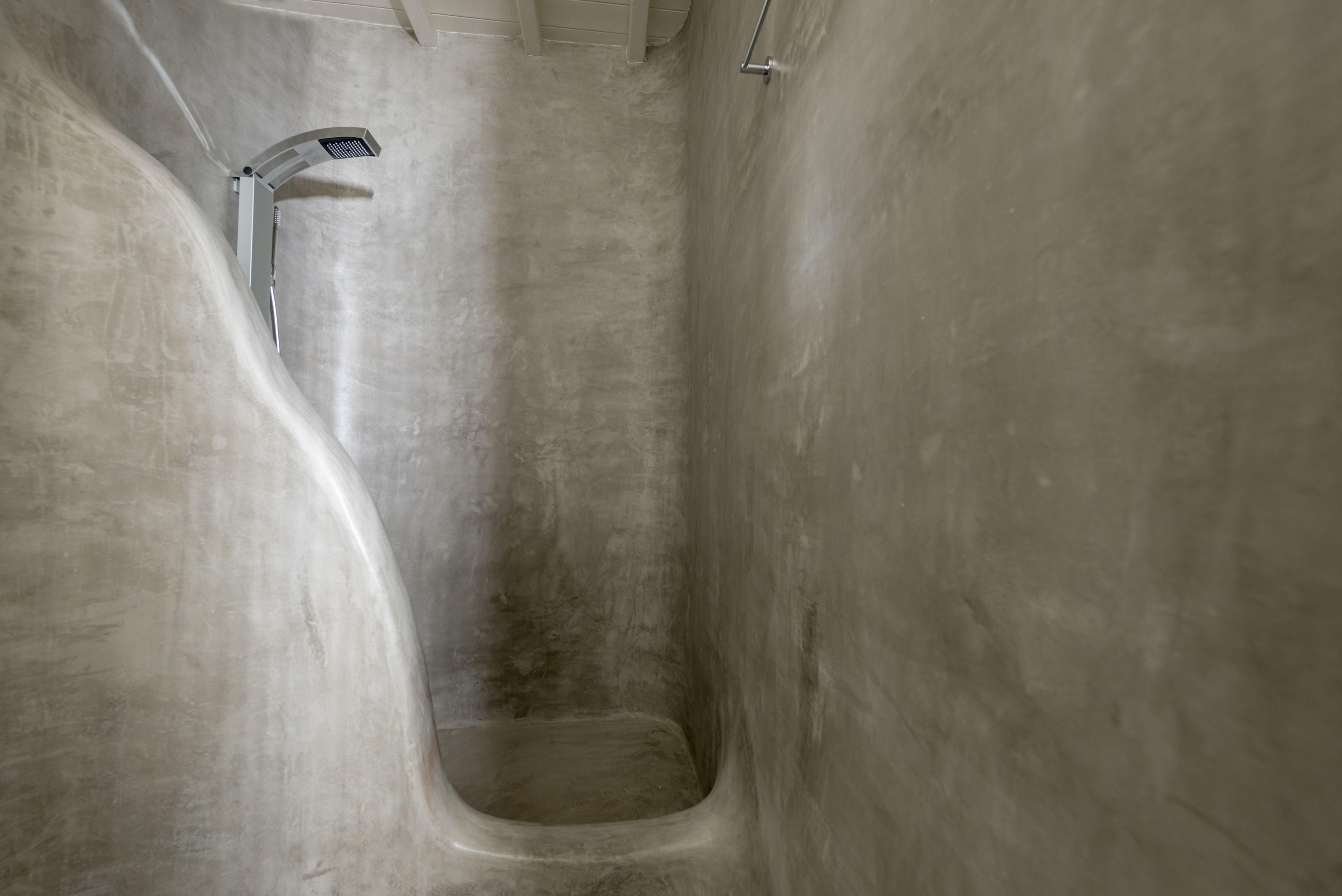 A narrow, concrete-walled bathroom with a single showerhead.