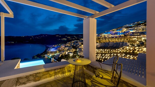A balcony with a table and chairs overlooking a coastal town at night. - Cova Mykonos Suites (Mykonos)