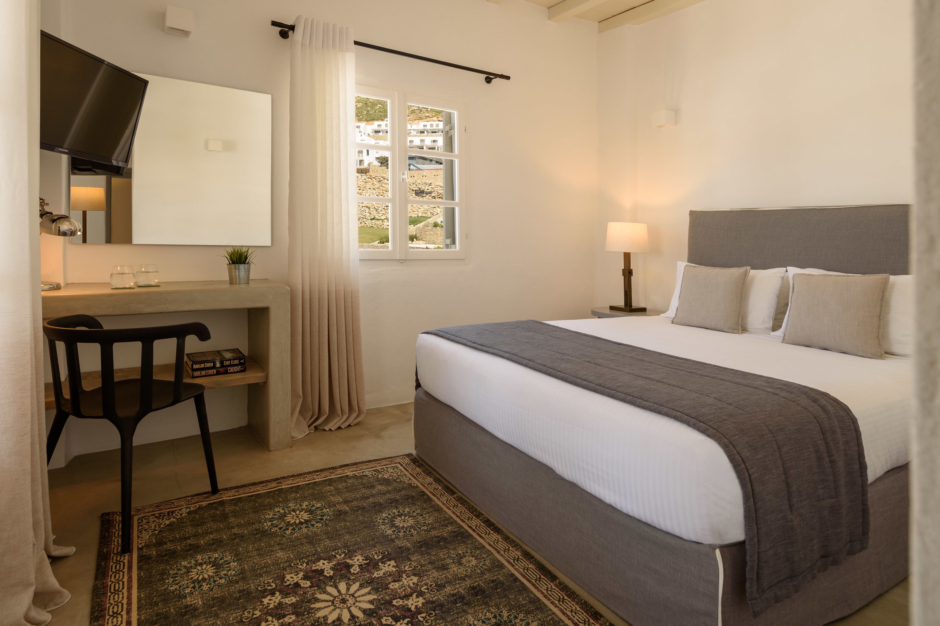 A bedroom with a bed, a desk, a chair, a window, and a lamp.
