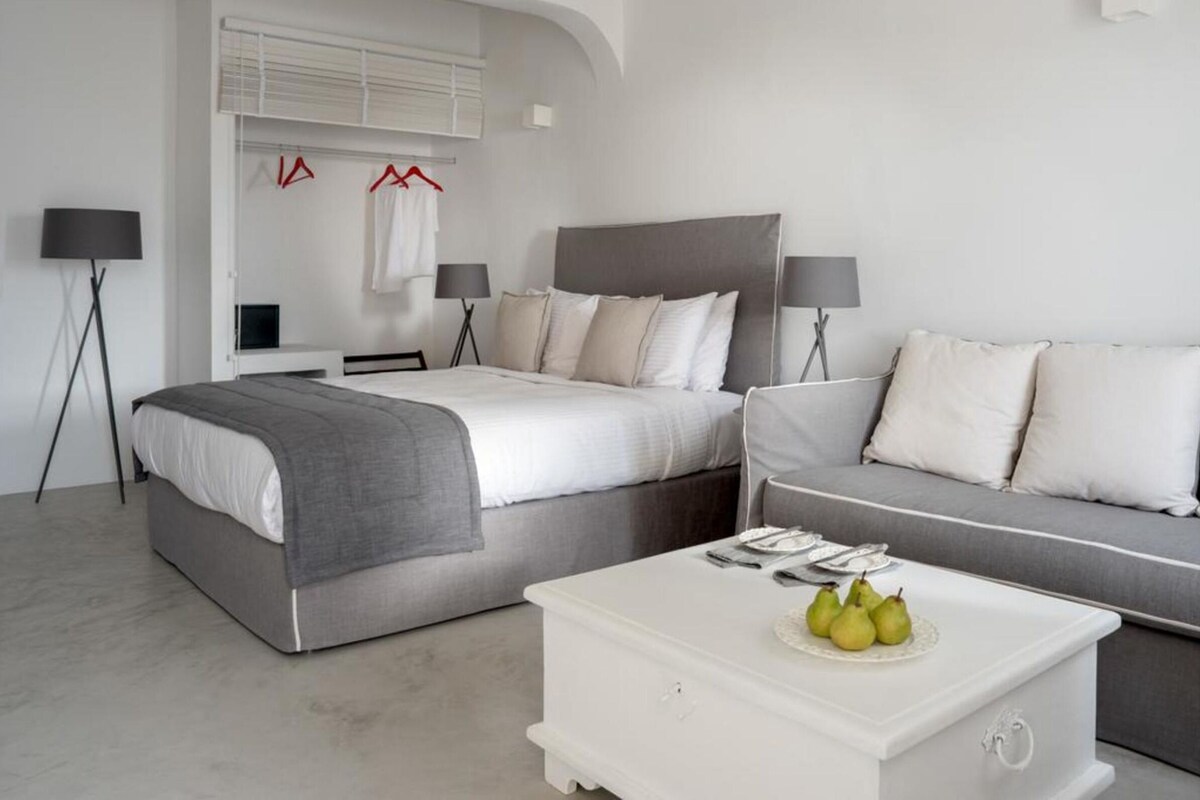 A modern hotel room with a bed, a sofa, a coffee table with fruit, and two lamps.