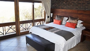 A bedroom with a large bed, a bench, a wooden headboard, and a view through a glass door. - Dinkweng Safari Camp (Vaalwater)