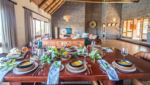 A dining area with a long wooden table set for a meal, surrounded by brick walls and wooden beams. - Dinkweng Safari Camp (Vaalwater)
