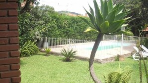 A backyard with a swimming pool, surrounded by a white fence, and various plants. - Pousada Nasa (São Bento do Sapucaí)