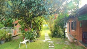 A garden pathway leading to a house with a brick exterior and a green awning. - Pousada Nasa (São Bento do Sapucaí)