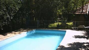 Piscina retangular com borda em azulejo, cercada por uma grade e vegetação exuberante.