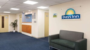 Un área de recepción con el letrero de Days Inn, un mostrador de recepción, una puerta a una sala privada y una planta.