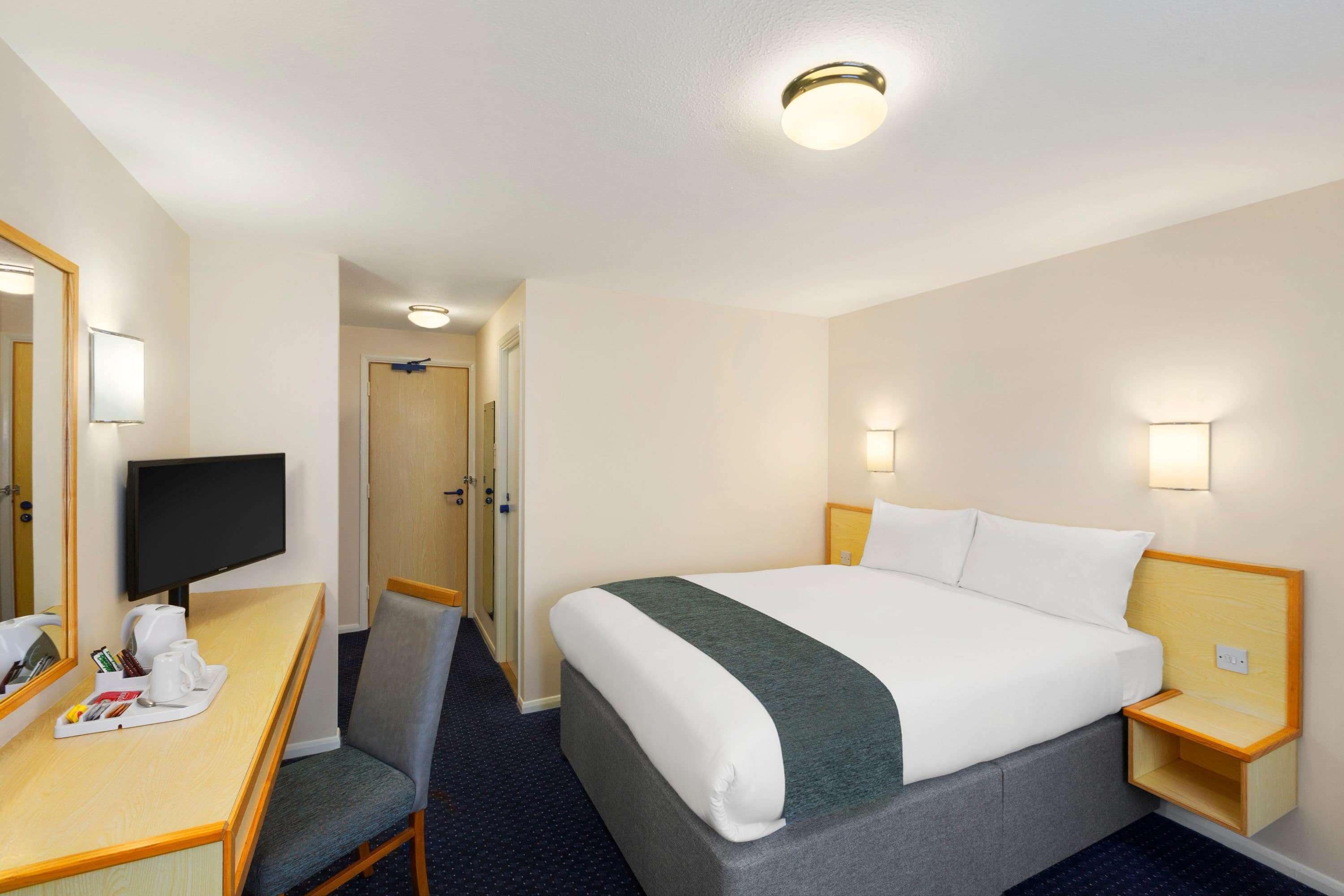 Ein Hotelzimmer mit Bett, Schreibtisch, Stuhl, Fernseher und einem kleinen Tisch mit Tablett.