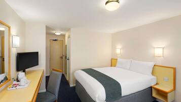 A hotel room with a bed, a desk, a chair, a television, and a small table with a tray of items.