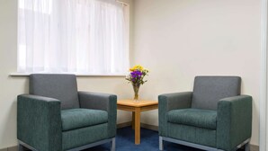 Una habitación con dos sillones grises, una mesita de madera con un florero y una ventana con cortinas translúcidas.