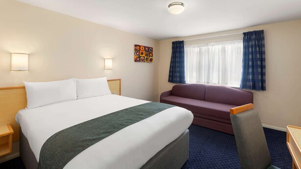 Habitación de hotel con una cama grande, un sofá, un escritorio y una ventana con cortinas.