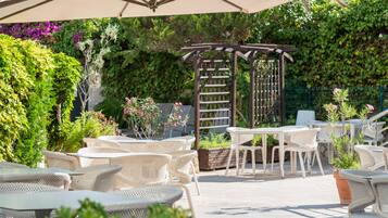 Une terrasse extérieure avec des tables et des chaises en osier, une pergola et une végétation luxuriante.