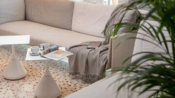 Una sala de estar moderna con un sofá color beige, almohadones a rayas, una mesa de centro con tazas y una revista, y una planta en maceta.