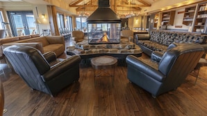 A cozy lounge area with leather sofas, a stone fireplace, and wooden beams.