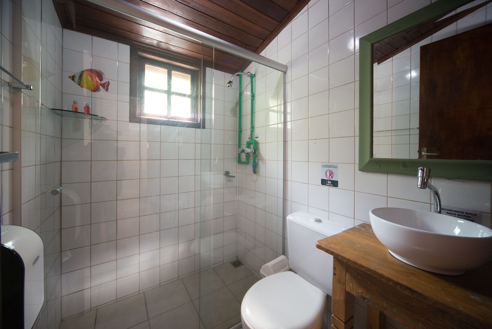 Un baño con cabina de ducha de vidrio, inodoro, lavabo con encimera de madera y espejo con marco verde.