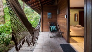 A hammock under a wooden roof, a bed with a pillow, and a view of greenery outside. - Pousada Treze Luas (Paranaguá)