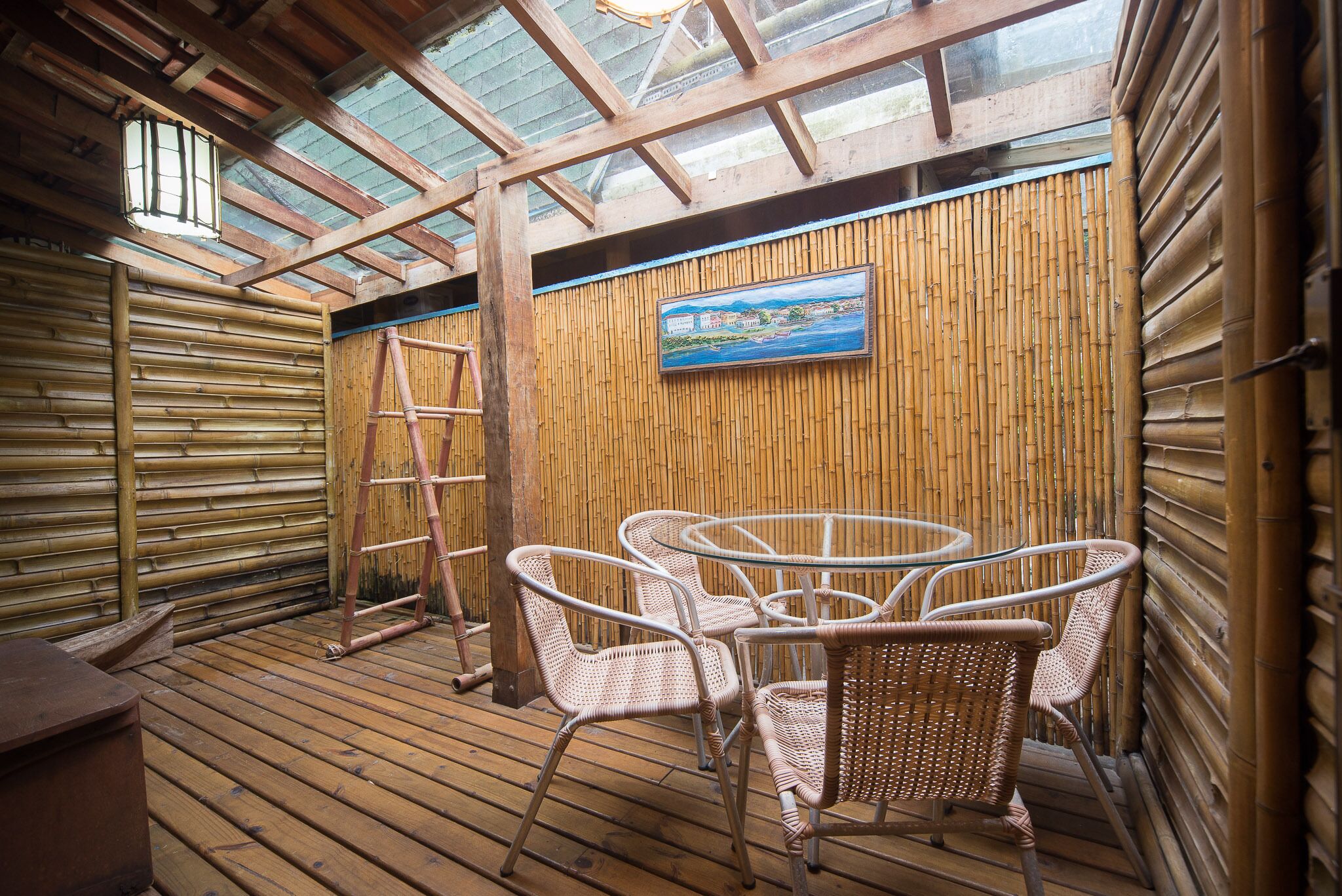 Una terraza de madera con sillas de mimbre y un cuadro de una escena costera.