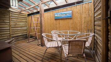 Una terraza de madera con sillas de mimbre y un cuadro de una escena costera.