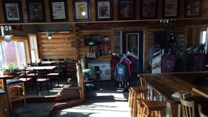 A rustic wooden interior with a bar area, dining tables, and a clothing rack. - Kohl's Resort (Bemidji)