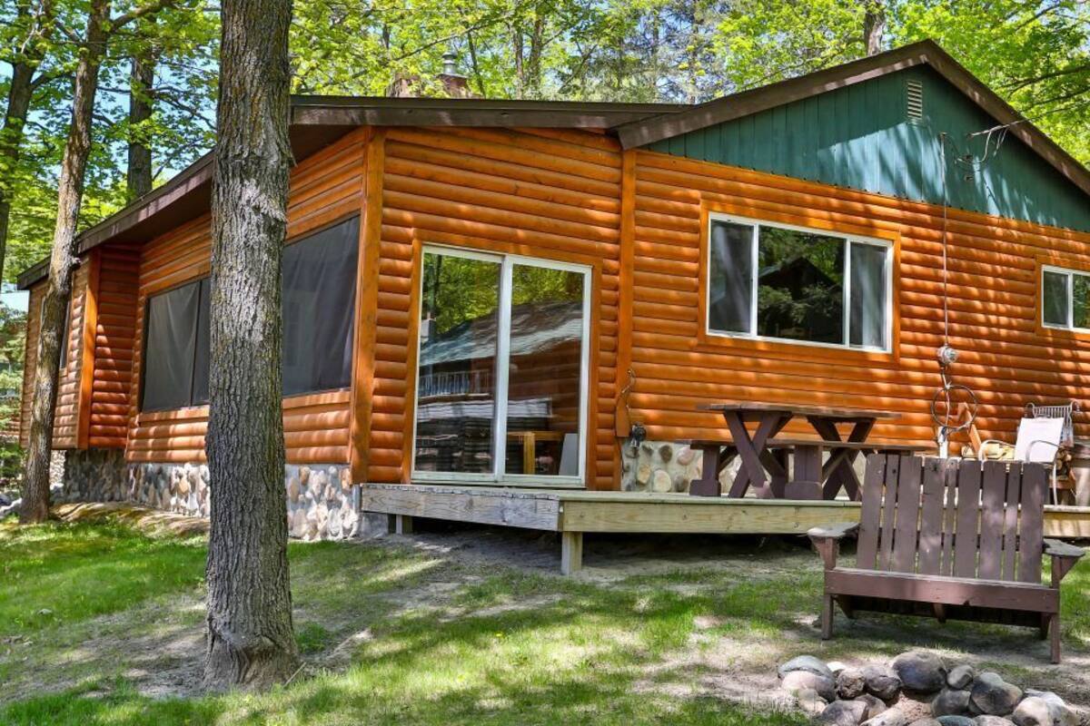 Una cabaña de madera con ventanas amplias, una terraza y una mesa de picnic.
