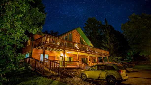 A two-story log cabin with a balcony, surrounded by trees, and a car parked in front. - Kohl's Resort (Bemidji)