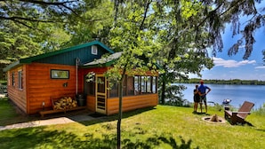 A cabin with a porch, a fire pit, and a view of a lake. - Kohl's Resort (Bemidji)