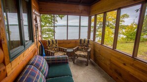 A wooden cabin with a bench and chairs by a large window overlooking a lake. - Kohl's Resort (Bemidji)