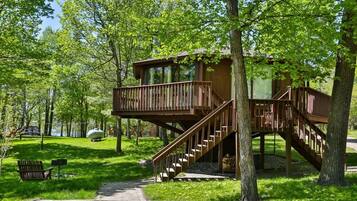Escape to a secluded treehouse cabin surrounded by a lush forest, featuring a balcony and staircase.