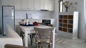 Eine kleine Küche mit weißen Schränken, einem Kühlschrank, einem Esstisch mit Stühlen und einem kleinen Blumentopf.