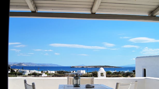 Eine Terrasse mit Tisch und Stühlen, mit Blick auf die Küste, Gebäude und das Meer.