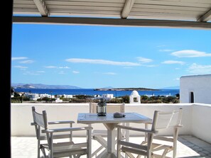 A terrace with a table and chairs, overlooking a coastal view with buildings and the sea.